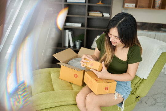 Young asian women unpacking awaited parce looking inside, sitting at sofa, unhappy customer opening cardboard box with online store order,Delivery service concept.