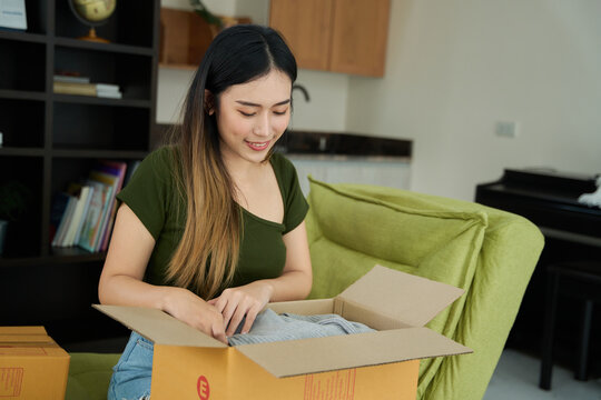 Young asian women unpacking awaited parce looking inside, sitting at sofa, unhappy customer opening cardboard box with online store order,Delivery service concept.