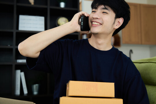 Young asian man unpacking  awaited parce looking inside, sitting at sofa, satisfied happy customer opening cardboard box with online store order, good shipping delivery service