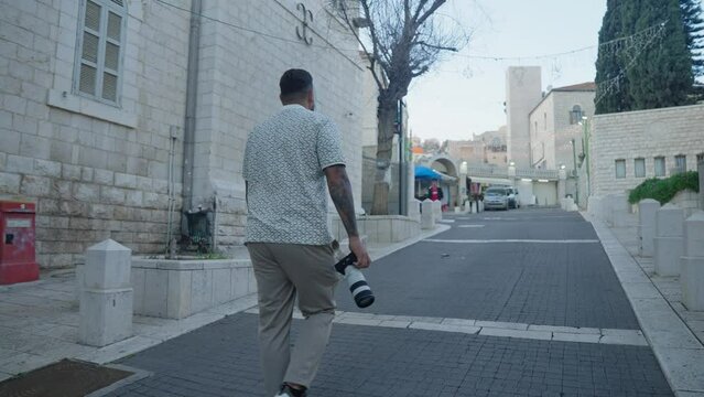 Man with camera and lens walks on cobble street in Nazareth, Israel