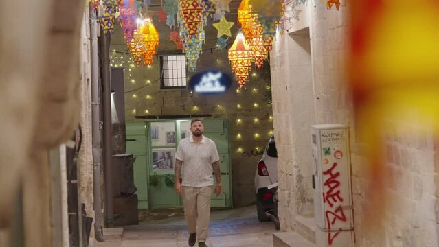 Bearded man walks under colourful patio lanterns in Nazareth alley
