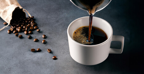 Hot Cup of Coffee Being Poured In to a white mug on an elegant table that has natural roasted beans from a bag