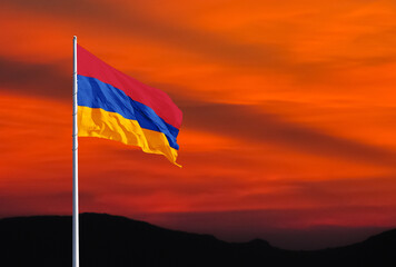 Waving Armenian flag against a red sky with clouds at sunset and empty space for text. Room for text.