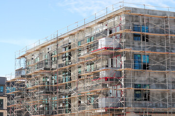 A low-angle exterior view of an apartment building under construction, with scaffolding and freshly plastered walls.