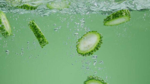Bitter melon (Momordica charantia) falling into the transparent water on white background and making air bubbles. Concept for food and lifestyle