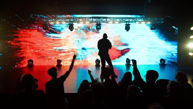 African-American Black rap artist performing his gig in front of a concert crowd on a stage of a large venue, surrounded by bright flashig lights