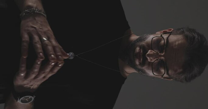 mysterious man in black t-shirt with glasses praying with palms together while standing in the flashlight in front of dark grey background
