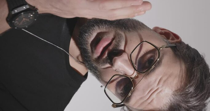 casual man with glasses wearing black t-shirt holding arms together and touching face in front of light grey background