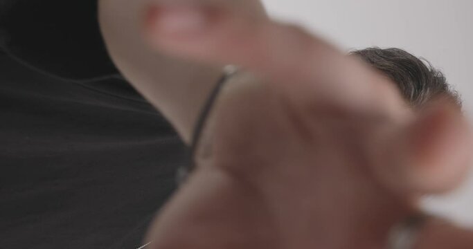 bearded stylish guy with glasses touching palms before covering camera with hands in front of light grey background