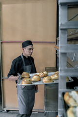 A young Hispanic baker is taking a tray full of cinnamon rolls from the oven