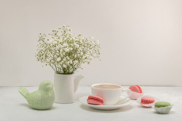 Coffee, colorful macaroons, a bouquet of gypsophila and a porcelain figurine of a bird on a white...