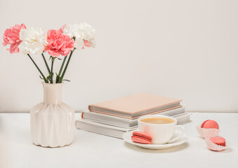 Coffee, pink macaroons, books and pink carnations on the table. Cozy breakfast.