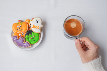woman hand holding coffee cup during eating funny Halloween Cookies. Happy Halloween day, Trick or Threat, Hello October, fall autumn, Traditional, party and holiday concept