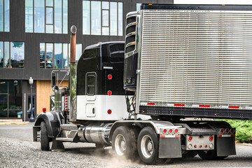 American idol classic bonnet big rig black semi truck tractor with refrigerated semi trailer running on the gravel road with dust from spinning wheels