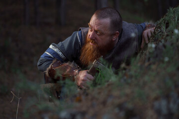 Naklejka na ściany i meble Lurking medieval red-haired viking warrior with beard with an ax in forest