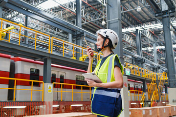 Female engineer wearing safety helmet and vest talking on radio while inspecting modern train...