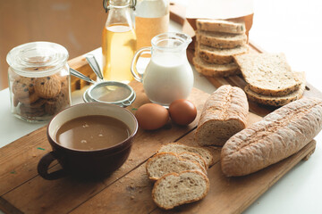 Different fresh breads, cookies, fresh milk and a glass of chocolate drink on the table in the morning sunlight shining through the window, view from above
