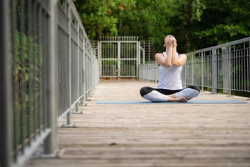 Fototapeta na wymiar Young female on a wooden bridge in the park with healthy yoga activities