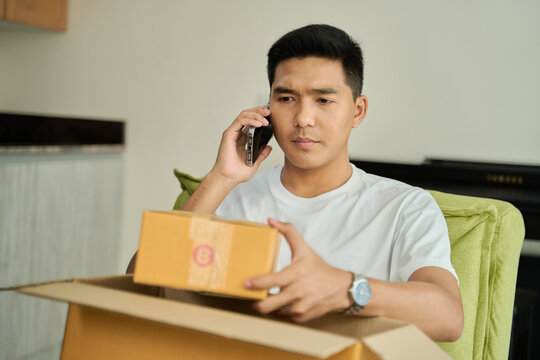 Young asian man unpacking awaited parce looking inside, sitting at sofa, unsatisfied customer opening cardboard box with online store order ,Delivery service concept.