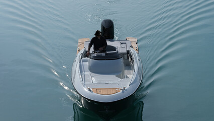 a man in a black hat is driving on a white boat with a motor front view. White boat with man slow...