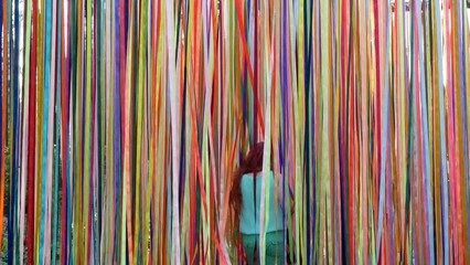 People going through the forest of colored ribbons that are flowing in the light breeze, selective focus. Festival or party decor and mood