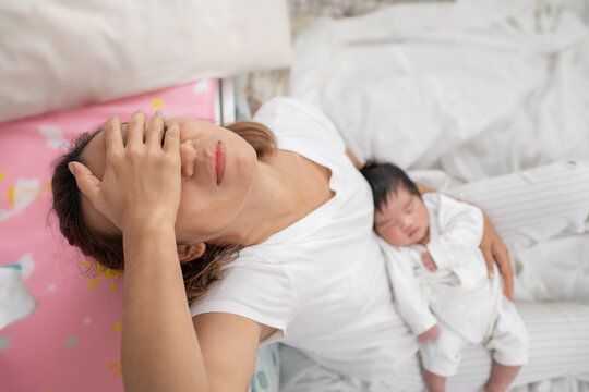 tired mother suffering from experiencing postnatal depression sitting on bed near children's cot. mother sleeping embracing to her asleep baby daughter sitting at home. single mom motherhood stressful