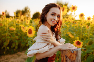 Smiling young woman with long brown hair in a field of yellow sunflower flowers at sunset