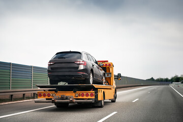 Tow truck with broken car on country road. Tow truck transporting car on the highway. Car service...