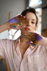 Creative portrait of young artist looking at camera through painted hands