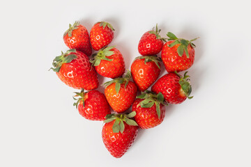 Whole ripe red strawberries are laid out in the form of a heart on a white background. Red ripe strawberries