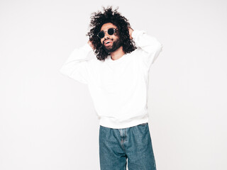 Handsome smiling hipster model. Unshaven Arabian man dressed in summer sweater and jeans clothes. Fashion male with long curly hairstyle isolated on white in studio. Copy space, mockup. In sunglasses