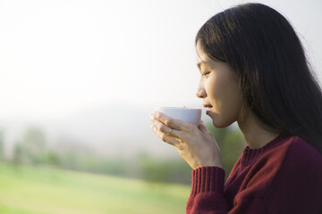Happy beautiful Asian young woman sitting on the grass field and enjoy relaxing with a stunning...