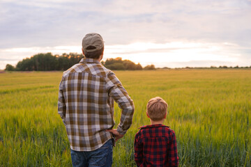 Farmer and his son in front of a sunset agricultural landscape. Man and a boy in a countryside field. Fatherhood, country life, farming and country lifestyle concept.