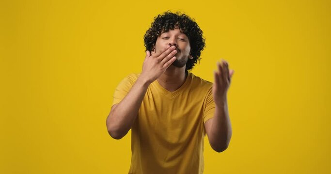 Young indian man giving air kiss and smiling looking at camera standing on orange studio background