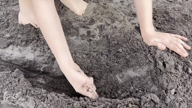 child digs a trench and play with sand on the beach 