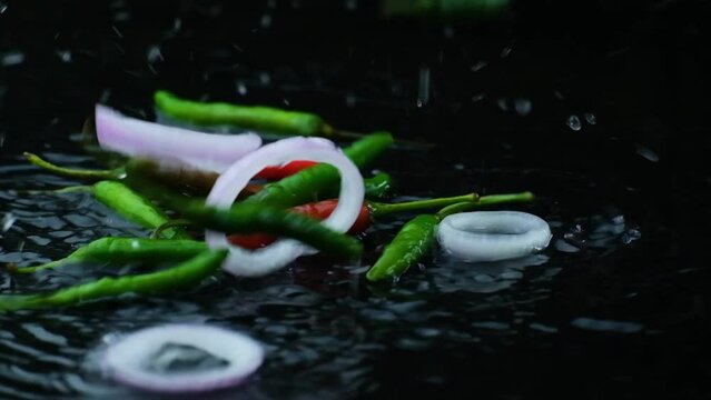 Freshly chopped green chili pepper, and sliced onion ring falling in the water. close up shot with black background