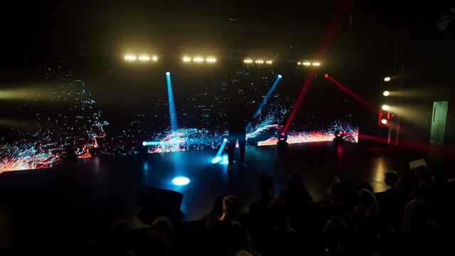 African-American Black rap artist performing his gig in front of a concert crowd on a stage of a large venue, surrounded by bright flashig lights