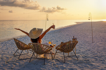 A elegant woman in a white dress enjoys the tropical sunset with a cocktail on a beach in the Maldives islands © moofushi