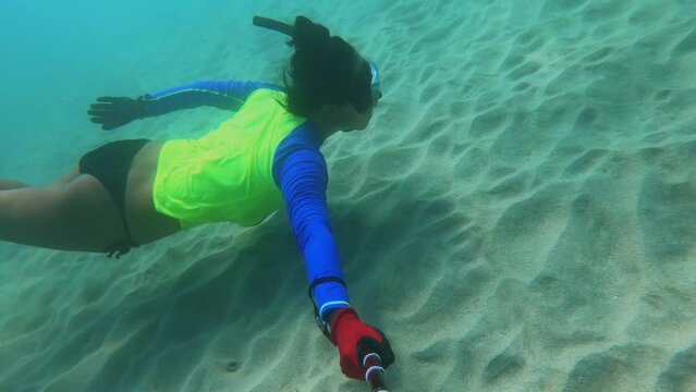 selfie of side view of an asian female free diver wearing bikini wet suit and snorkel mask in the ocean water diving swimming kicking fins holding breath at the sandy sea bed with no creatures fishes