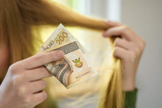 Usługi fryzjerskie, polski banknot 200 pln trzymany na tle pasma włos&oacute;w 