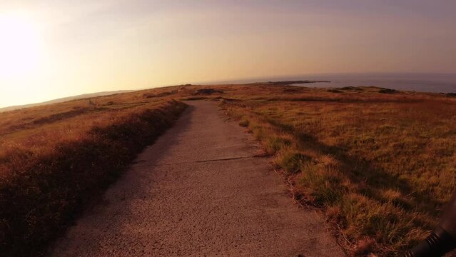 moving forward scooter riding view 
 on road of dry deserted grass bush land at Dung Lung Cliff with horizon ocean line with calm sea water at back with clouds blue sky during sunset afternoon