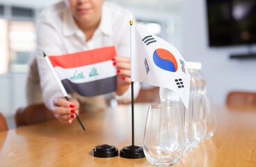 Closeup of national flags of Iraq and South Korea in hands of female office secretary preparing table in meeting room for international negotiations. Concept of diplomatic relations