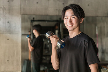 スポーツジムでダンベル・鉄アレイを使って腕を鍛える筋トレをするアジア人男性
