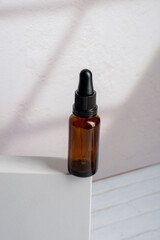 cosmetic bottles made of dark amber glass on white background with palm leaves shadow.