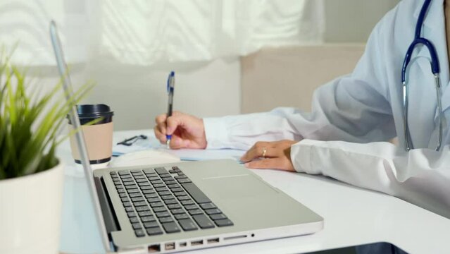 Closeup of doctor or nurse woman in uniform with stethoscope typing information of patient prescription from paperwork medical history form into laptop computer for record document data report