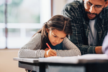 Young girl writing with a colouring pen with the help of her teacher - Powered by Adobe