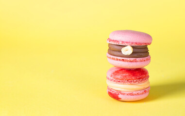 Pink macarons with hazelnuts and caramel on yellow background, Copy space