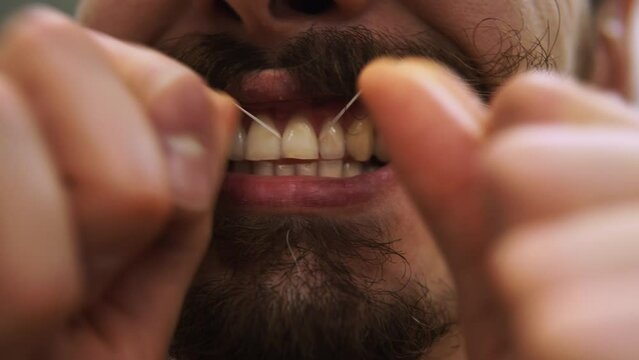 Caucasian man with curly moustache is cleaning teeth with floss filmed in macro. Closeup footage of male young adult person making dental hygiene staying in bathroom in the morning. Healthcare theme