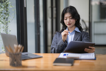 Attractive business asian woman using a digital tablet while sitting in workplace desk in an office.