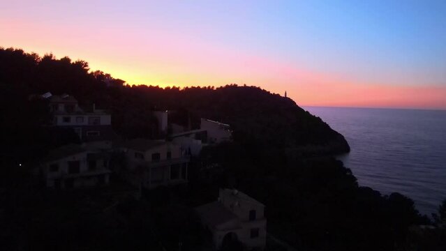 Lighthouse silhouette at sunset on tropical island Soller Mallorca Spain on hot summer evening with colour in the sky dramatic aerial drone shot